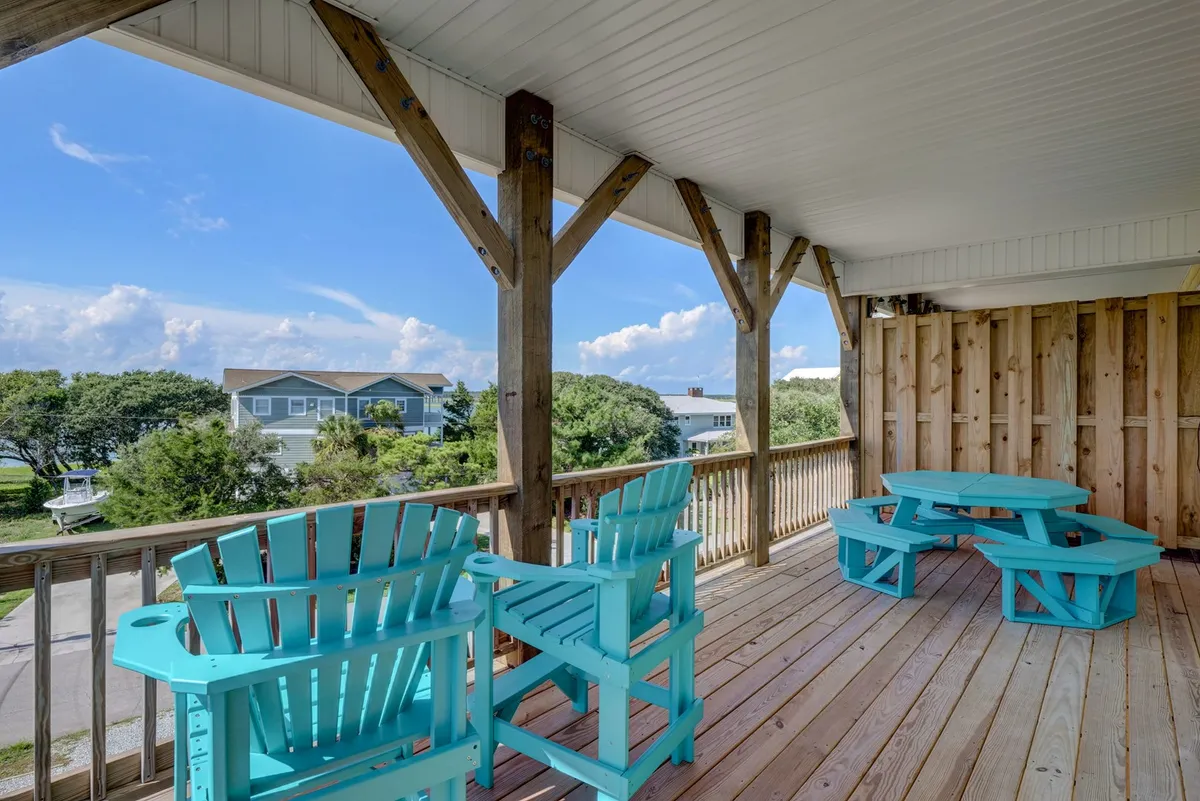 A wooden deck with turquoise Adirondack chairs overlooking a neighborhood filled with greenery. The deck is perfect for relaxing, socializing, or enjoying a sunset after a day at the beach, bridging the connection between outdoor adventures and downtime with friends.