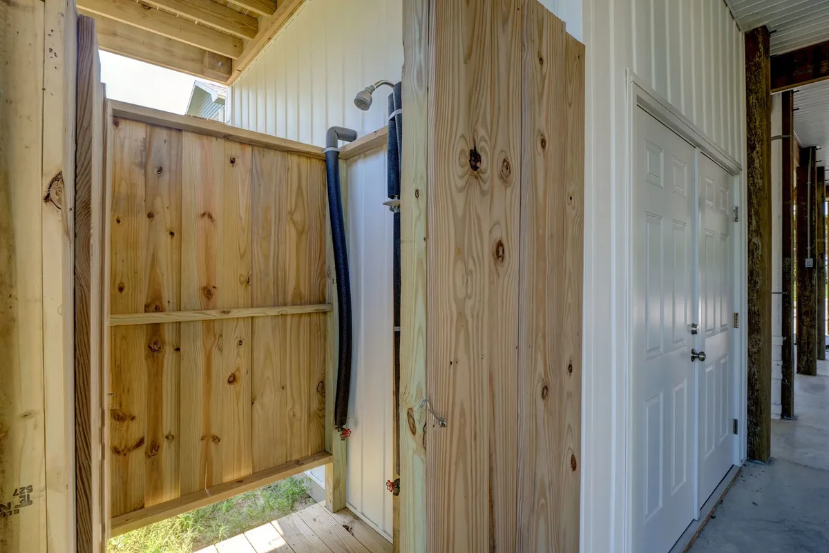 This image features the home's enclosed outdoor shower, with sturdy wooden walls and a simple doorway, set just outside the living area. The natural light and textured wood give the space a fresh, inviting feel—a perfect place to rinse away salt and sand after a day on the beach.