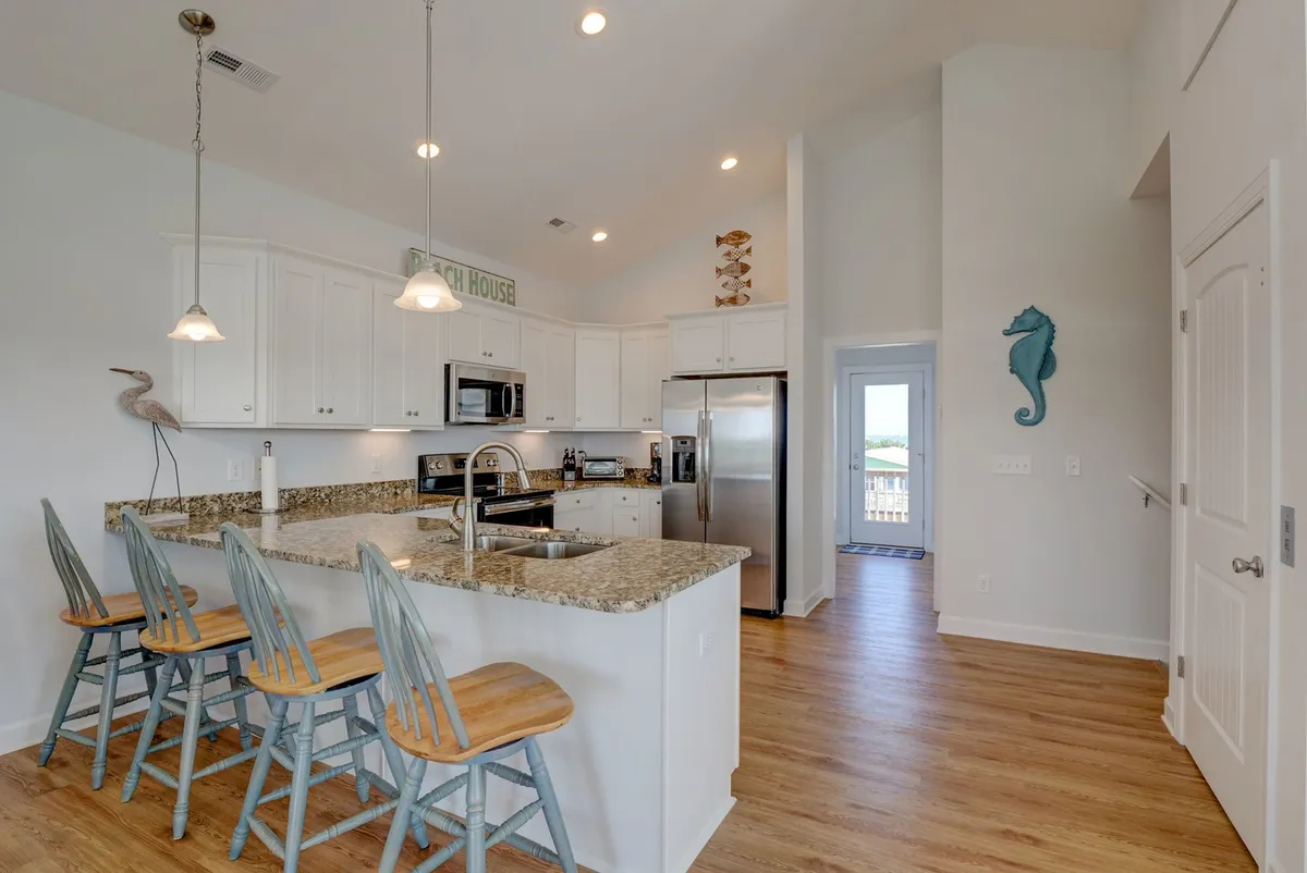 A modern kitchen scene featuring a central island with bar stools, up-to-date stainless steel appliances, and beach-themed decor. The layout encourages both cooking and conversation, with plenty of room for multiple cooks or family members to gather.